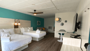 Modern hotel room with two white beds and blue accent wall.