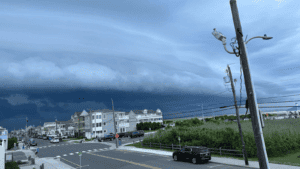Dark storm clouds gather over a coastal town with white buildings and a parked black truck.