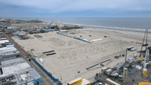 A large sandy beach with volleyball courts and blue fencing near the ocean.