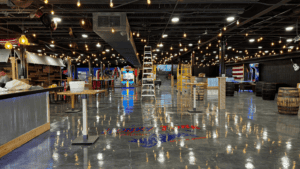 Interior of a large, open warehouse with reflective floors and hanging lights.
