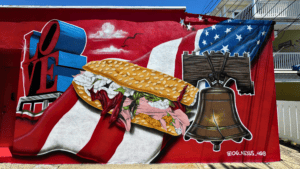 A vibrant mural featuring a submarine sandwich, American flag, Liberty Bell, and Statue of Liberty's torch.