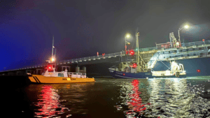 A boat passing under a raised bridge at night with reflections on the water.