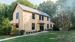 A modern wooden house with large windows and a well-kept lawn.