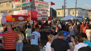 Crowded outdoor food market with various food stalls and people.