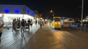 People walking on a lit boardwalk at night with parked yellow trams.