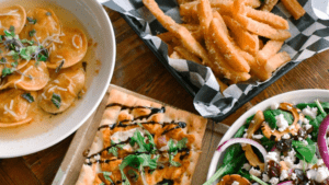 A close-up of grilled chicken with fries and salad on a wooden table.