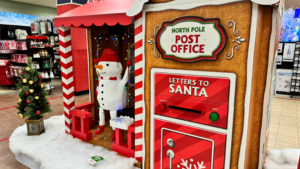 A festive snowman stands outside a North Pole Post Office with a mailbox for letters to Santa.