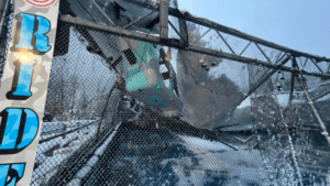 A damaged metal fence with a torn mesh and a green bucket caught in it.