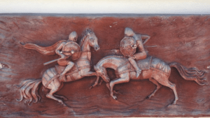 Wooden carving of two warriors on horseback in combat.