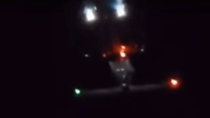 A dark image showing an aircraft with illuminated lights at night.