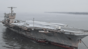 A large aircraft carrier docked on a foggy day with a tugboat alongside.