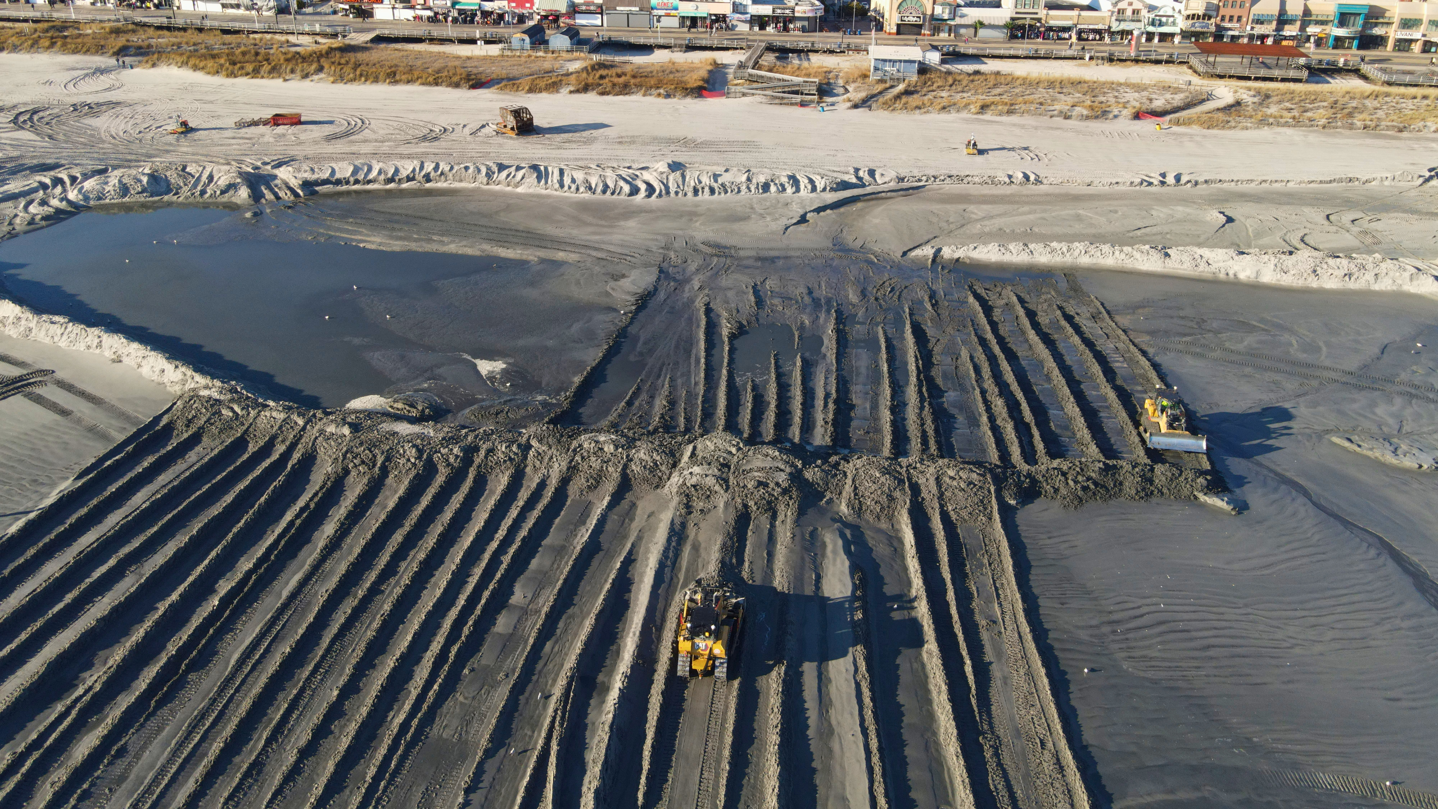 A bulldozer working on a beach with exposed rock formations.