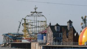 A cloudy day at a seaside amusement park with a roller coaster and old buildings.