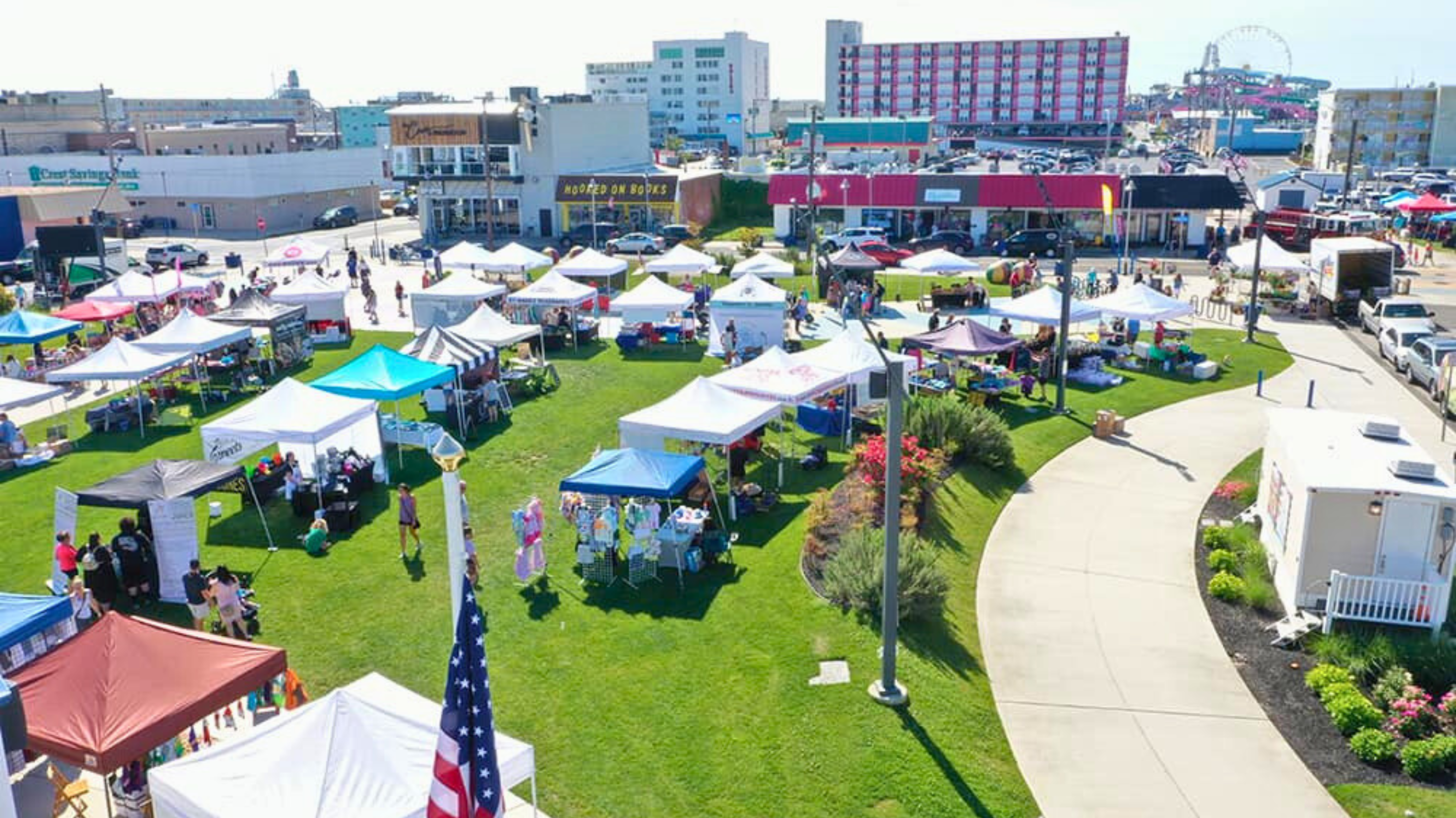 A vibrant outdoor market with white tents and American flags on a sunny day.