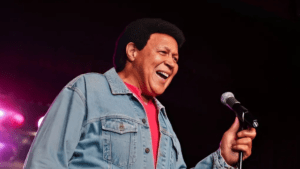 A man singing joyfully into a microphone wearing a denim jacket.