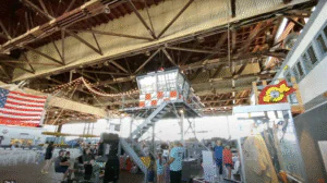 A group of people interacting around a large industrial machine inside a warehouse.