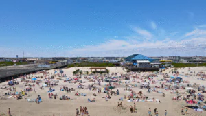 Crowded beach with people enjoying a sunny day under a clear blue sky.