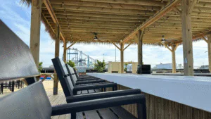 A row of black chairs under a wooden pergola near the beach.