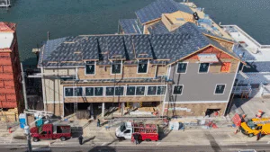 A house under construction with roofers working and a red truck parked outside.