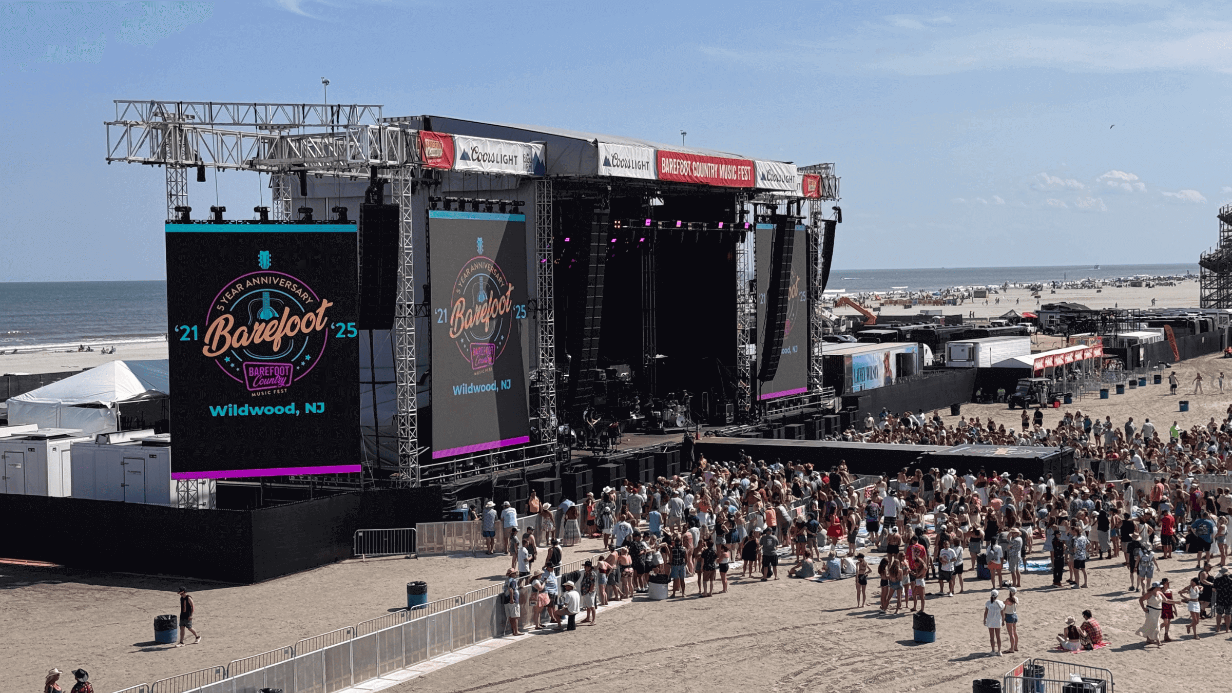 Beachside concert stage with crowd gathering.