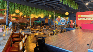A vibrant restaurant interior with hanging plants, wooden tables, and colorful wall art.