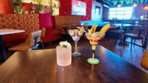 Three colorful cocktails on a wooden table in a cozy bar.