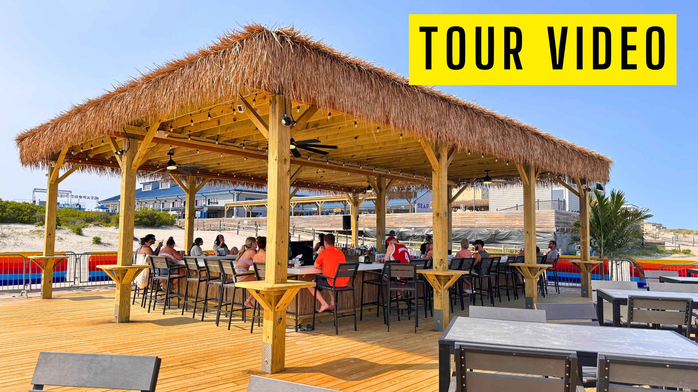 Outdoor seating area under a thatched roof with people dining.