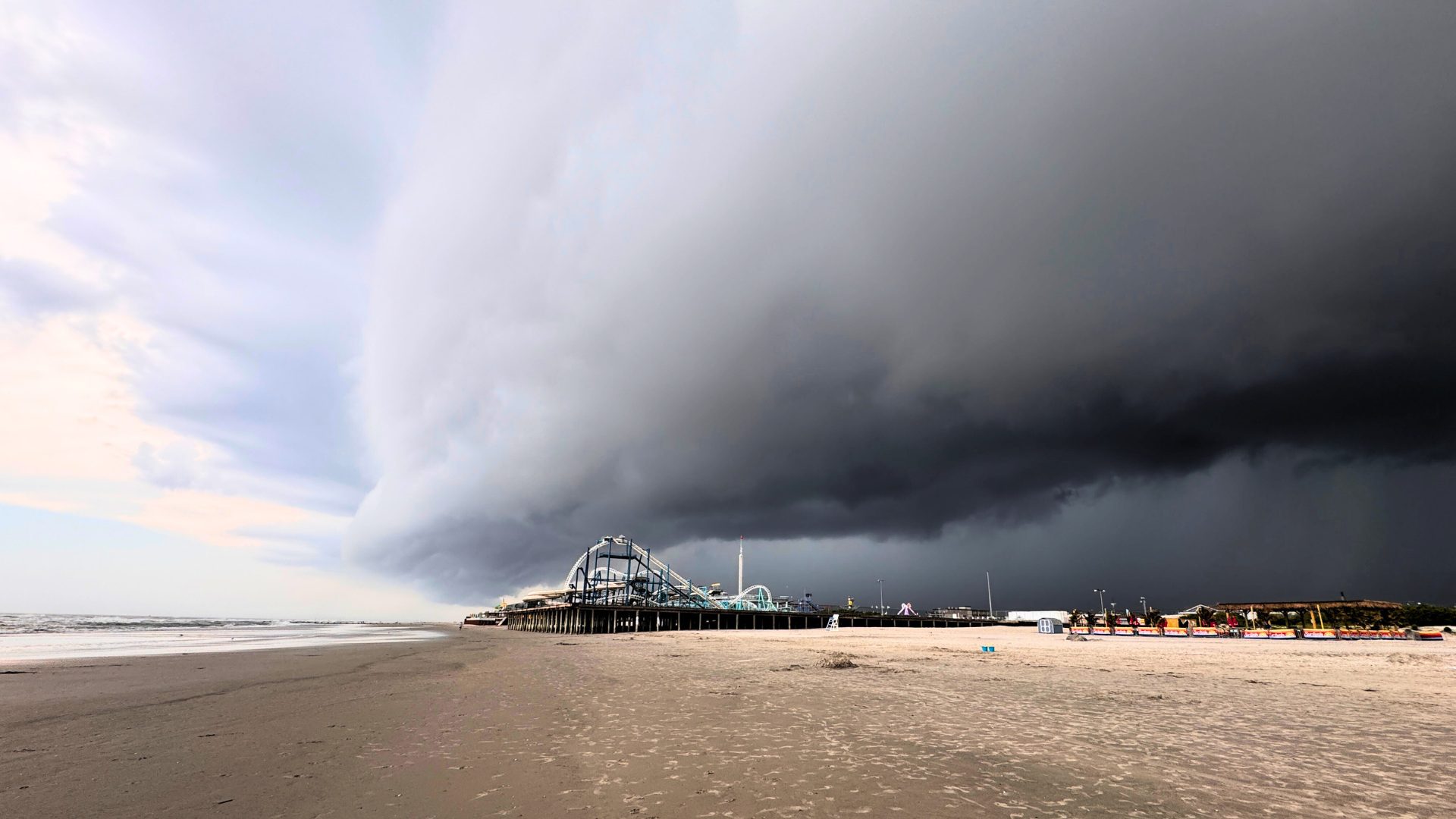 Dark storm clouds over beach and pier.