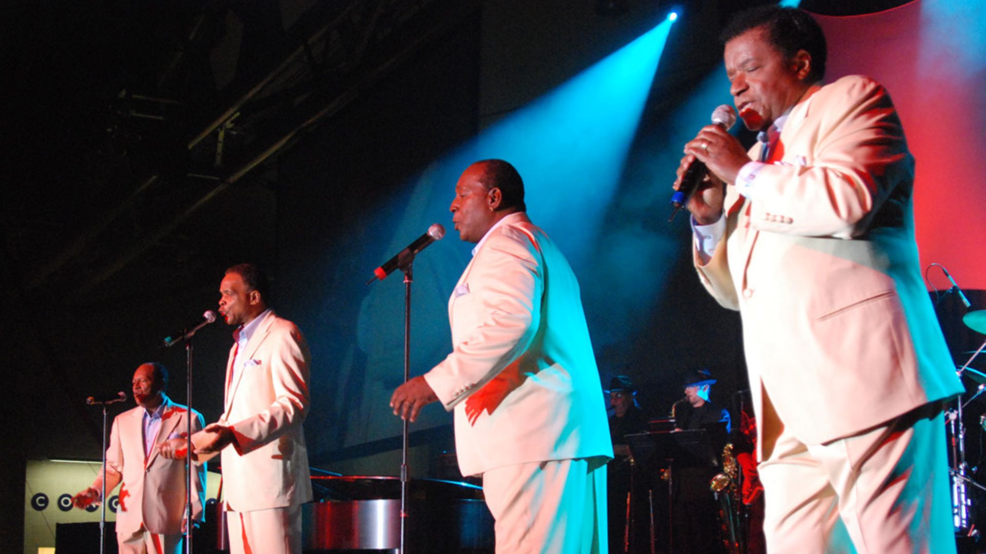 Four men singing on stage in suits.